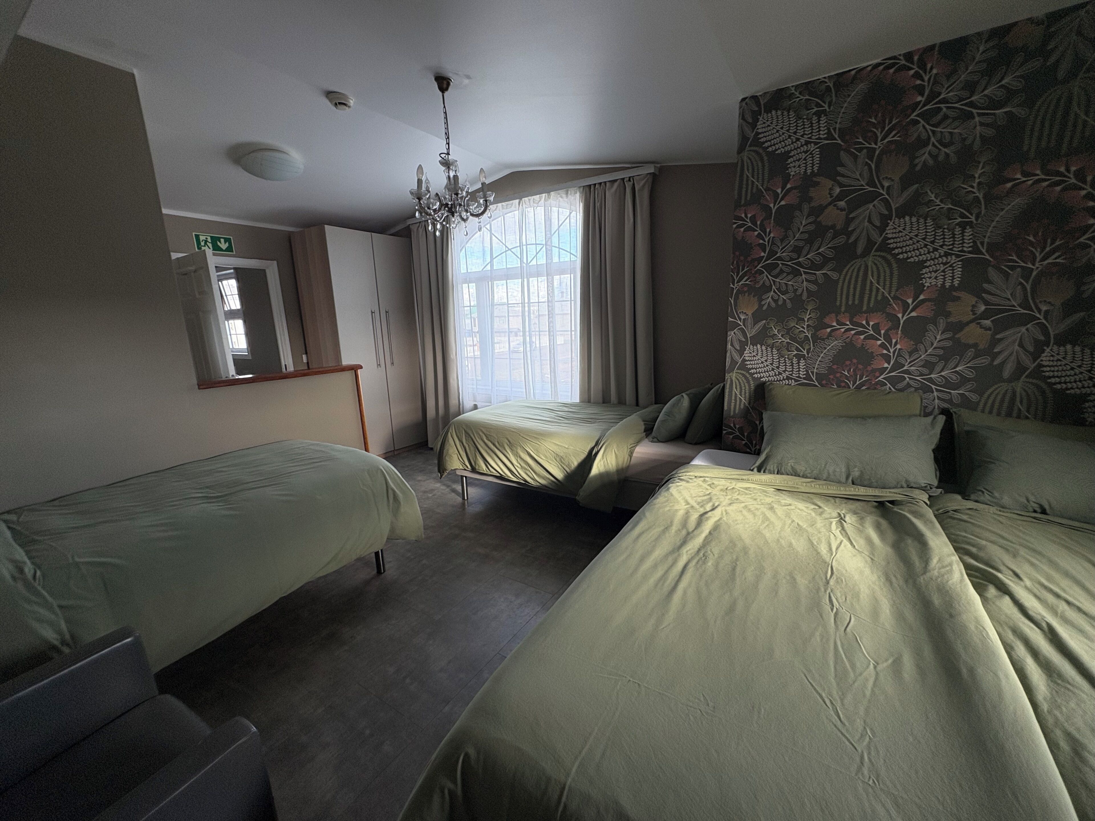 Habitación de hotel con dos camas individuales, un armario, un espejo y una ventana con cortinas.