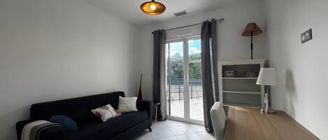Un salón moderno con un sofá negro, una mesa de centro de madera, una lámpara y vistas a través de un ventanal corredero.