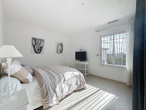 Un dormitorio con una cama, un televisor sobre un mueble bajo y obras de arte en la pared.