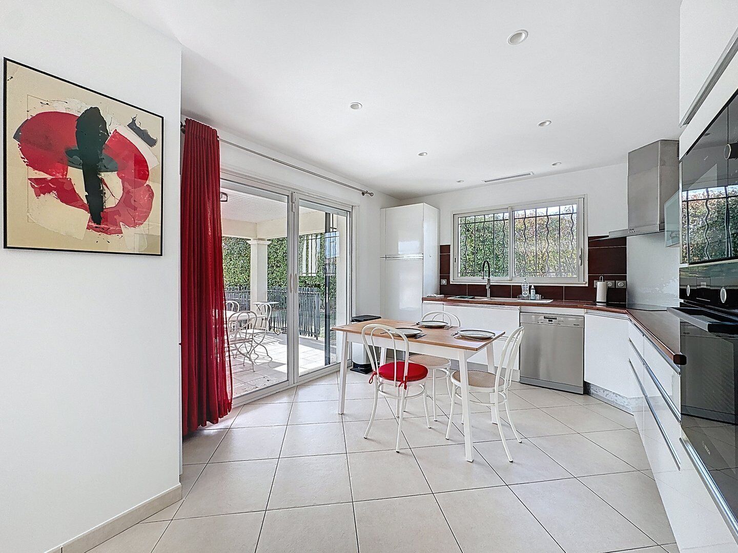 A modern kitchen with white cabinets, a dining area with a table and chairs, and a large window with a view of greenery.
