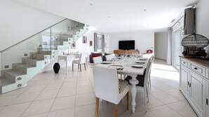 Moderni olohuone, jossa on ruokailutila, portaikko ja litteänäyttöinen televisio.