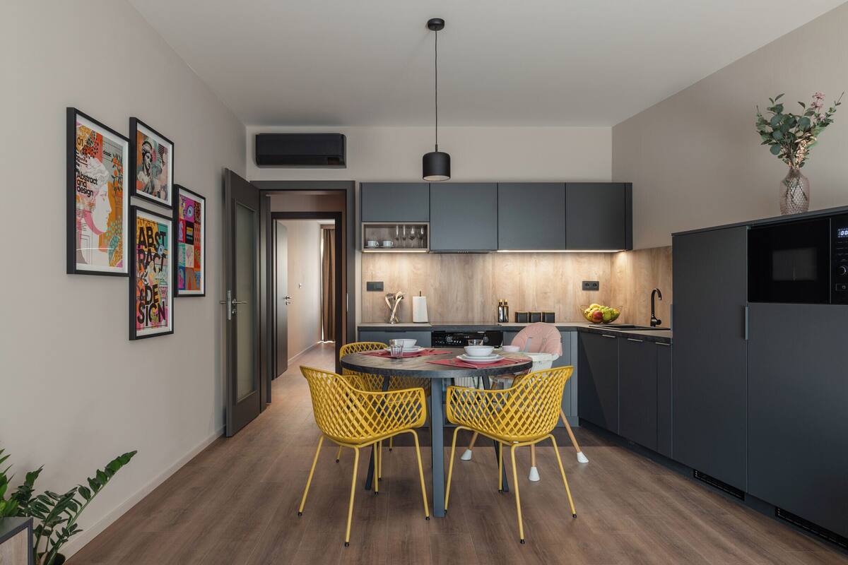Cocina moderna con armarios oscuros, una isla central y sillas amarillas.