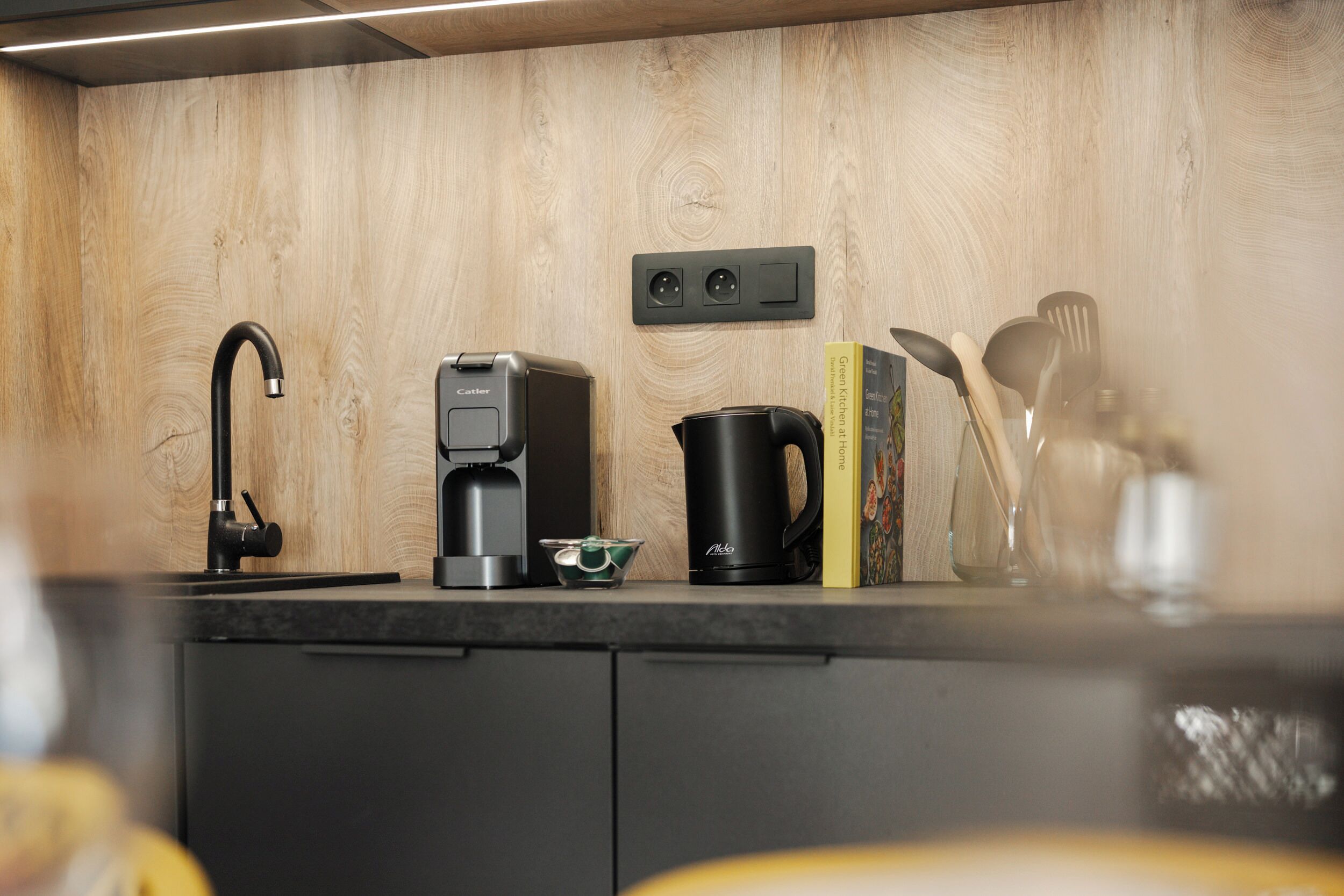 Ett modernt kök med en svart kaffebryggare, en vattenkokare och en kaffekanna på bänkskivan.