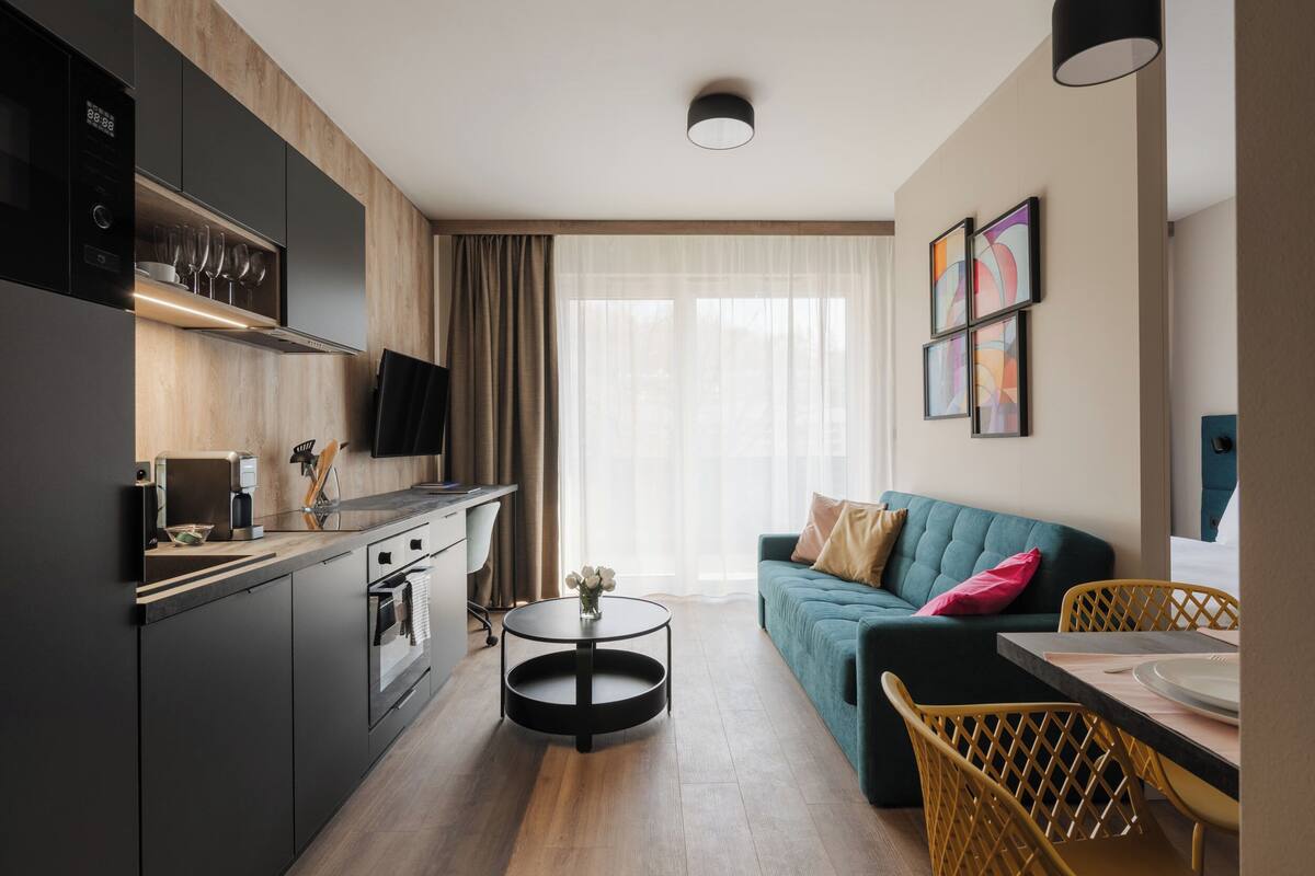 Una cocina moderna con horno empotrado y microondas, un comedor con una mesa redonda y sillas, y una sala de estar con sofá y televisor.