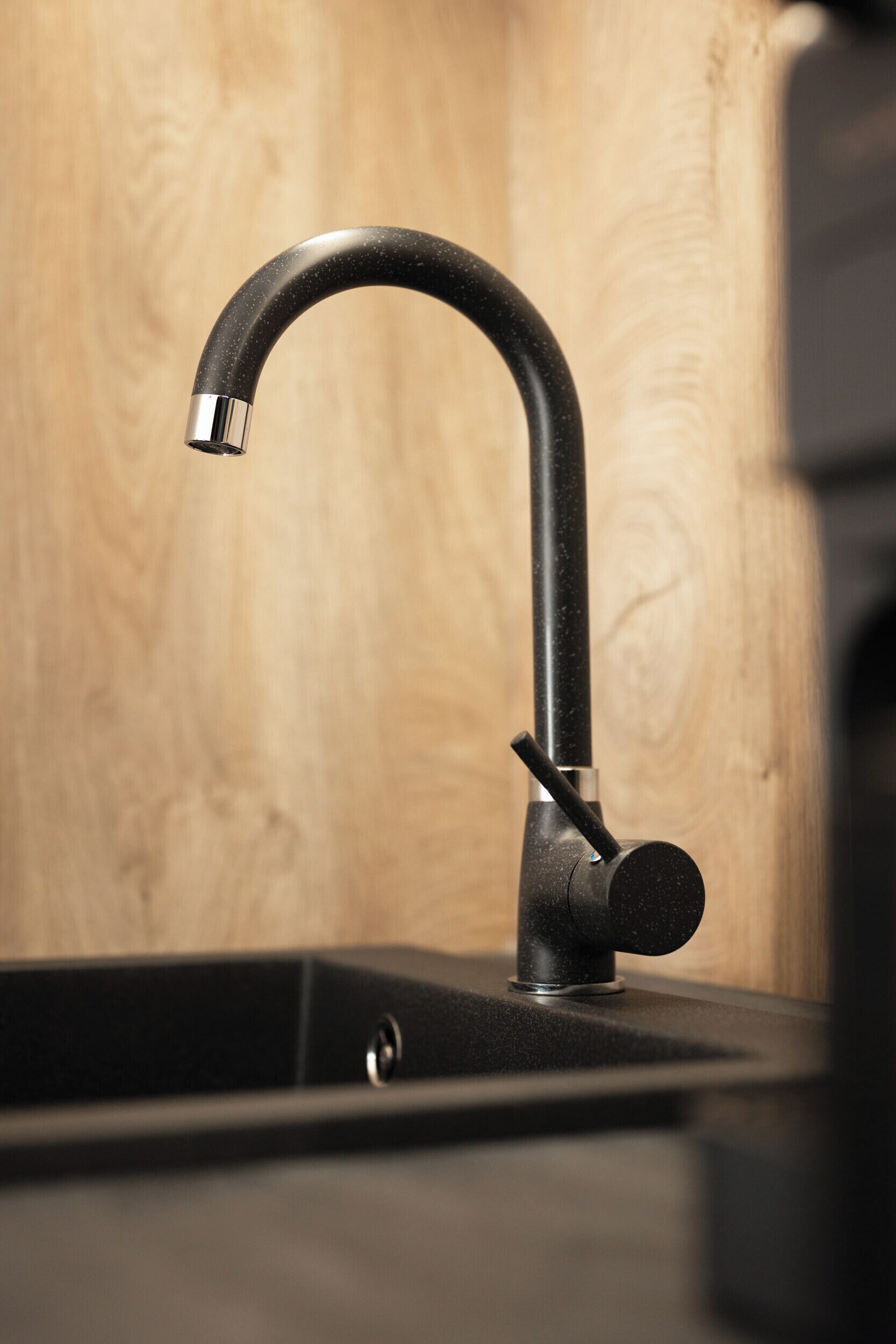A modern kitchen with a sleek black faucet, a wooden backsplash, and a black countertop.