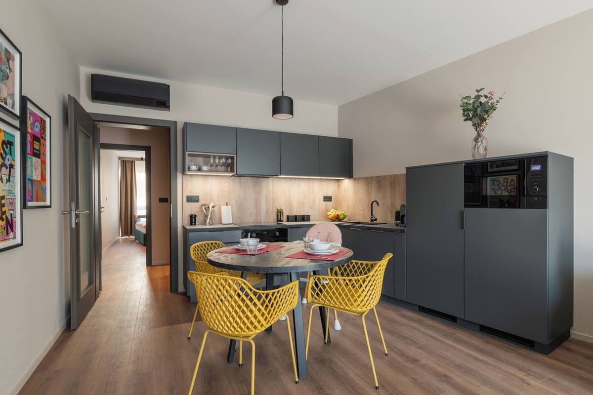 Una cocina moderna con una isla central, sillas amarillas y armarios grises.