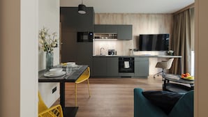 A modern kitchen with grey cabinets, a built-in oven, and a dining area with a yellow chair.