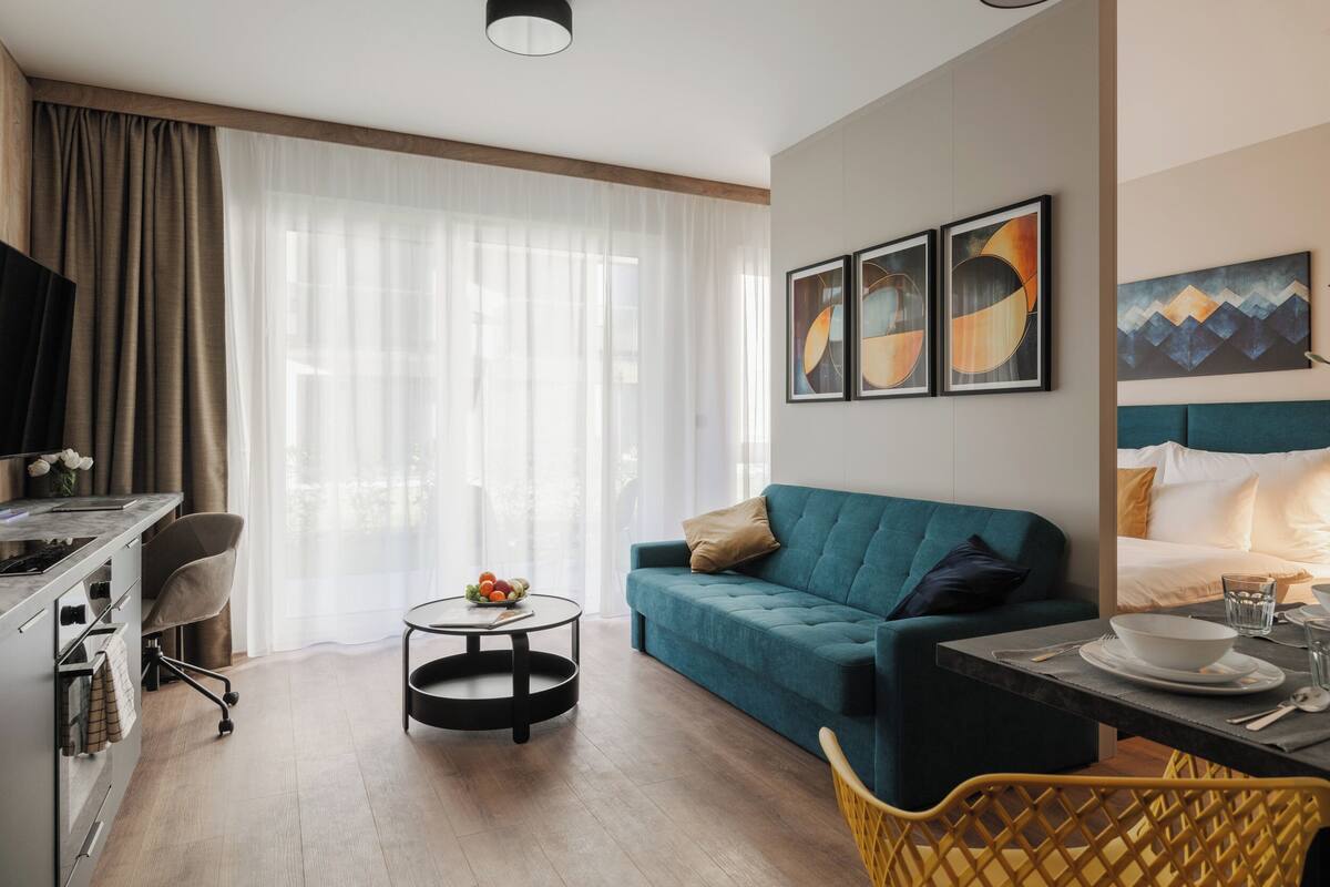 Una sala moderna con un sofá color turquesa, una mesa de comedor y una zona de cocina con televisor y una silla.