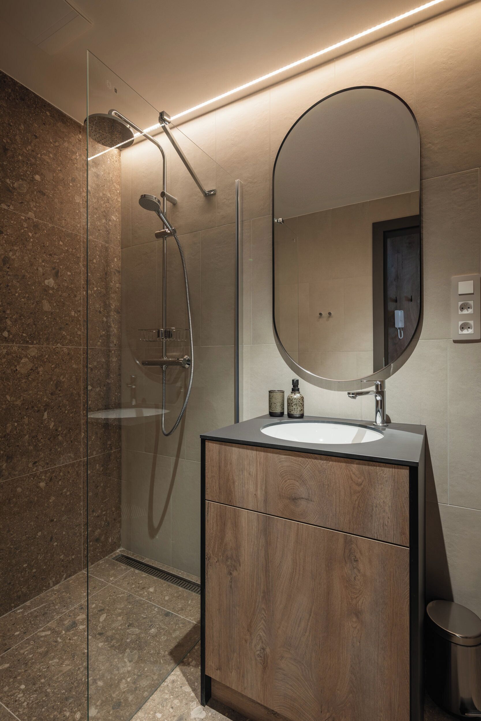A modern bathroom with a glass-enclosed shower, a wooden vanity, and a large mirror.