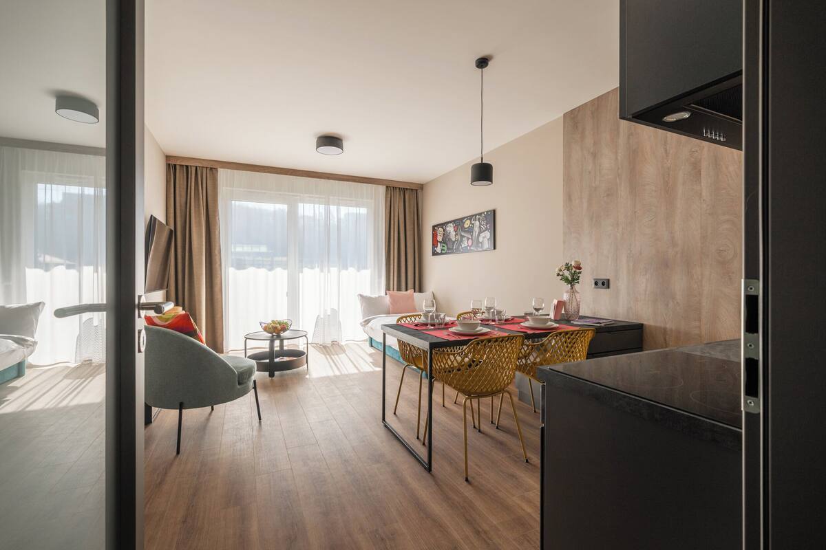 Una sala de estar moderna con comedor, piso de madera y un ventanal con cortinas traslúcidas.