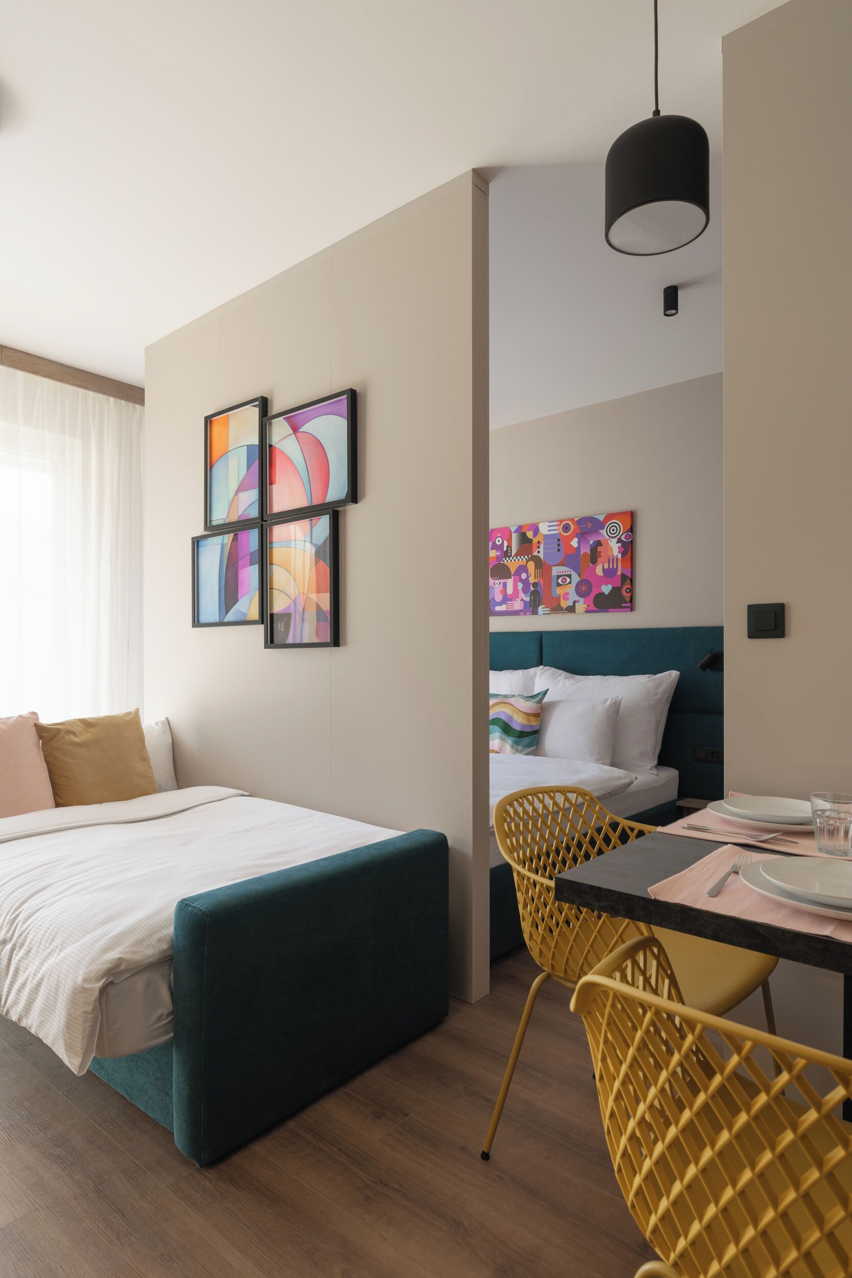 Una camera d'albergo moderna con un letto, un'area pranzo con sedie gialle e opere d'arte alle pareti.