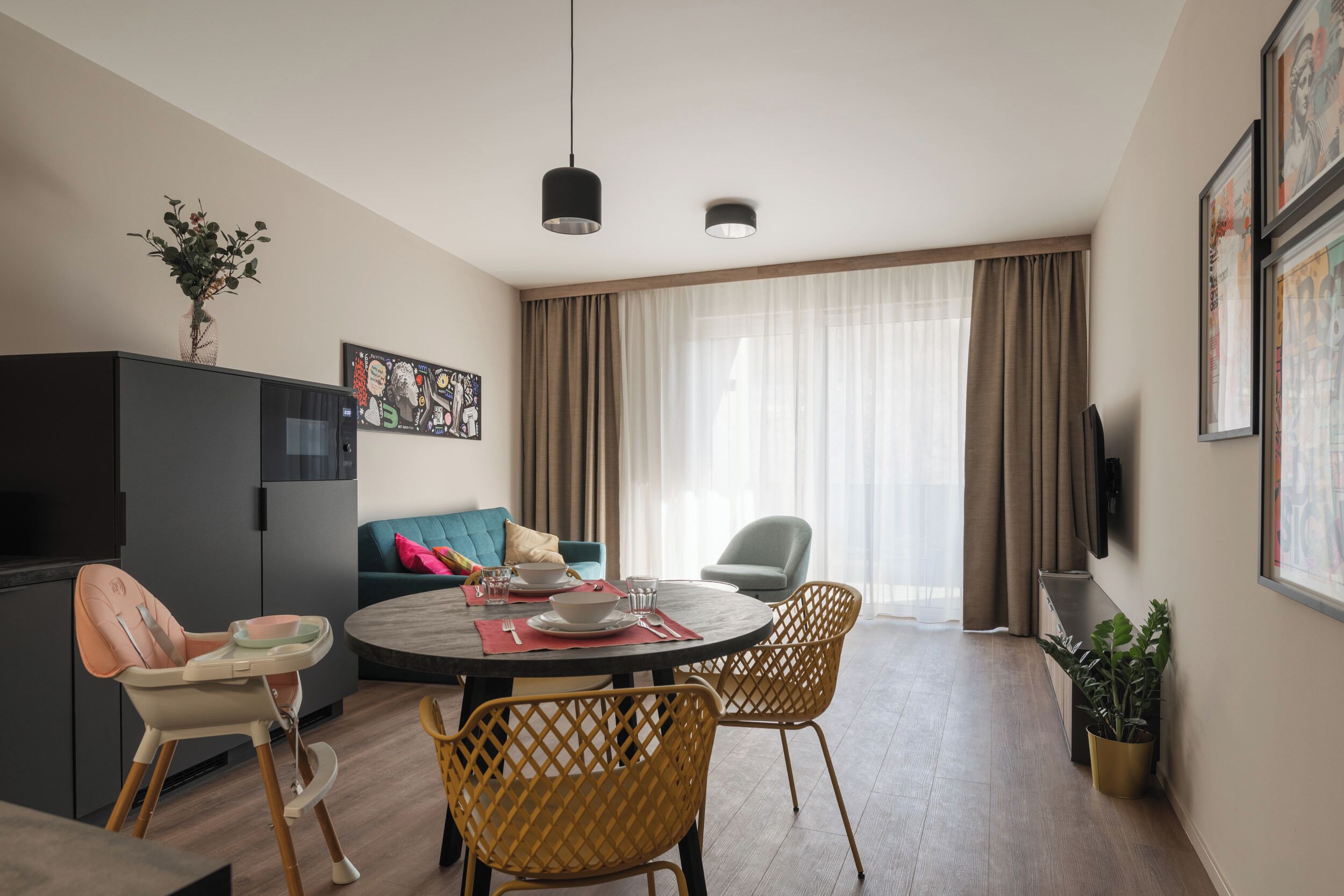 Una sala de estar moderna con una mesa de comedor, sillas, un sofá, un televisor y un gran ventanal con cortinas.