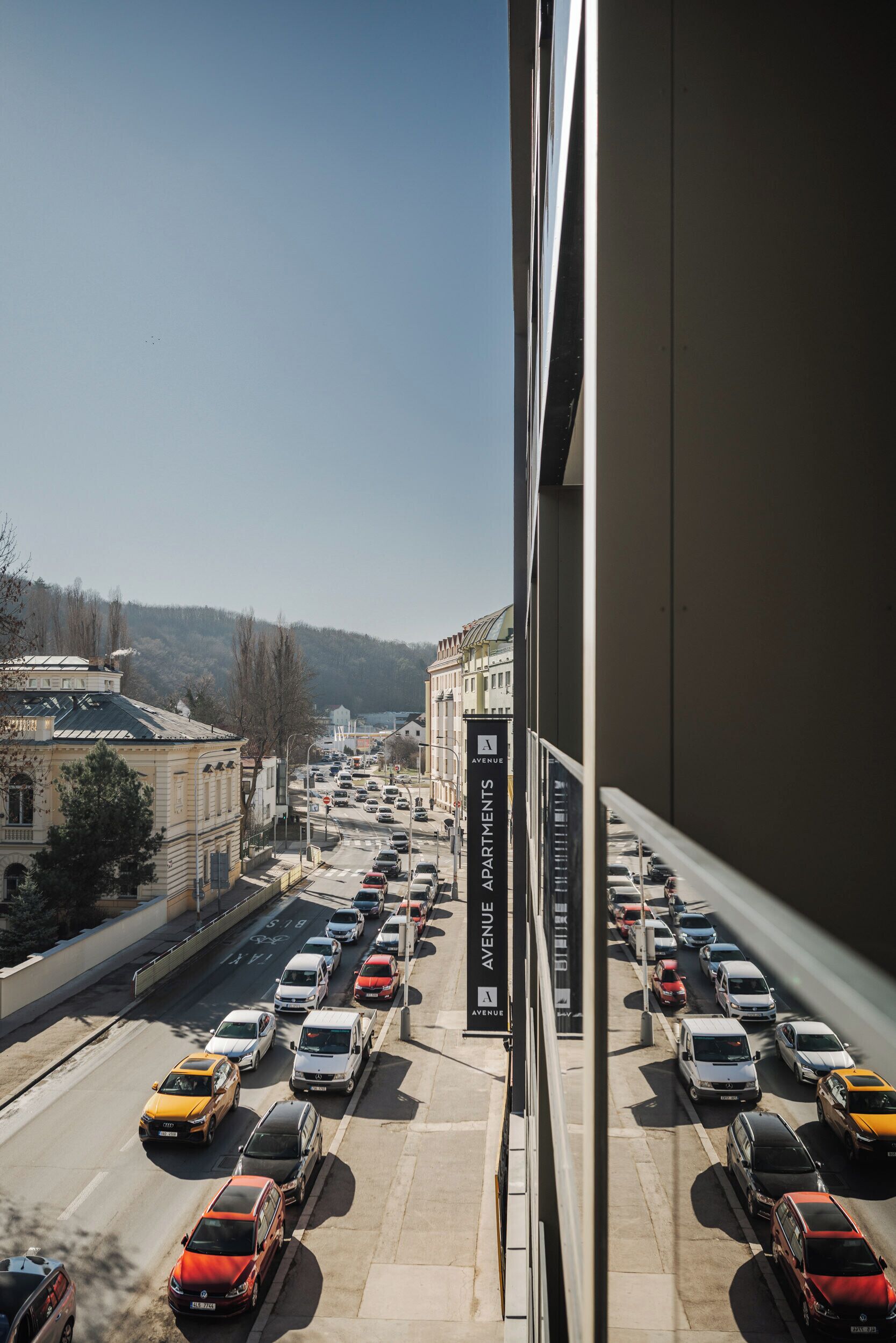 Uma rua urbana movimentada com várias faixas de trânsito e um edifício com a placa 'Avenue Apartments'.