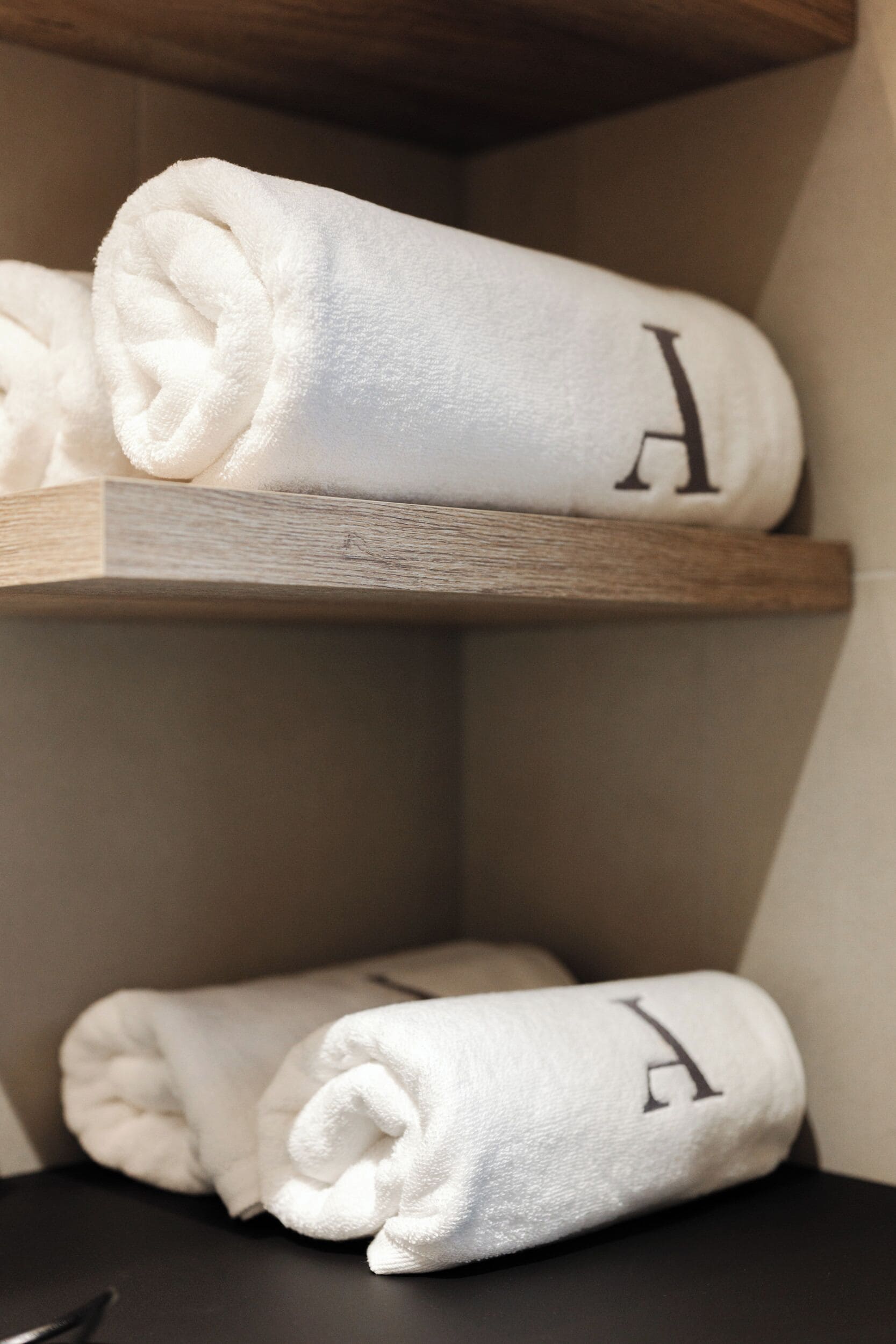 A corner of a room with two white towels rolled up and placed on a wooden shelf.