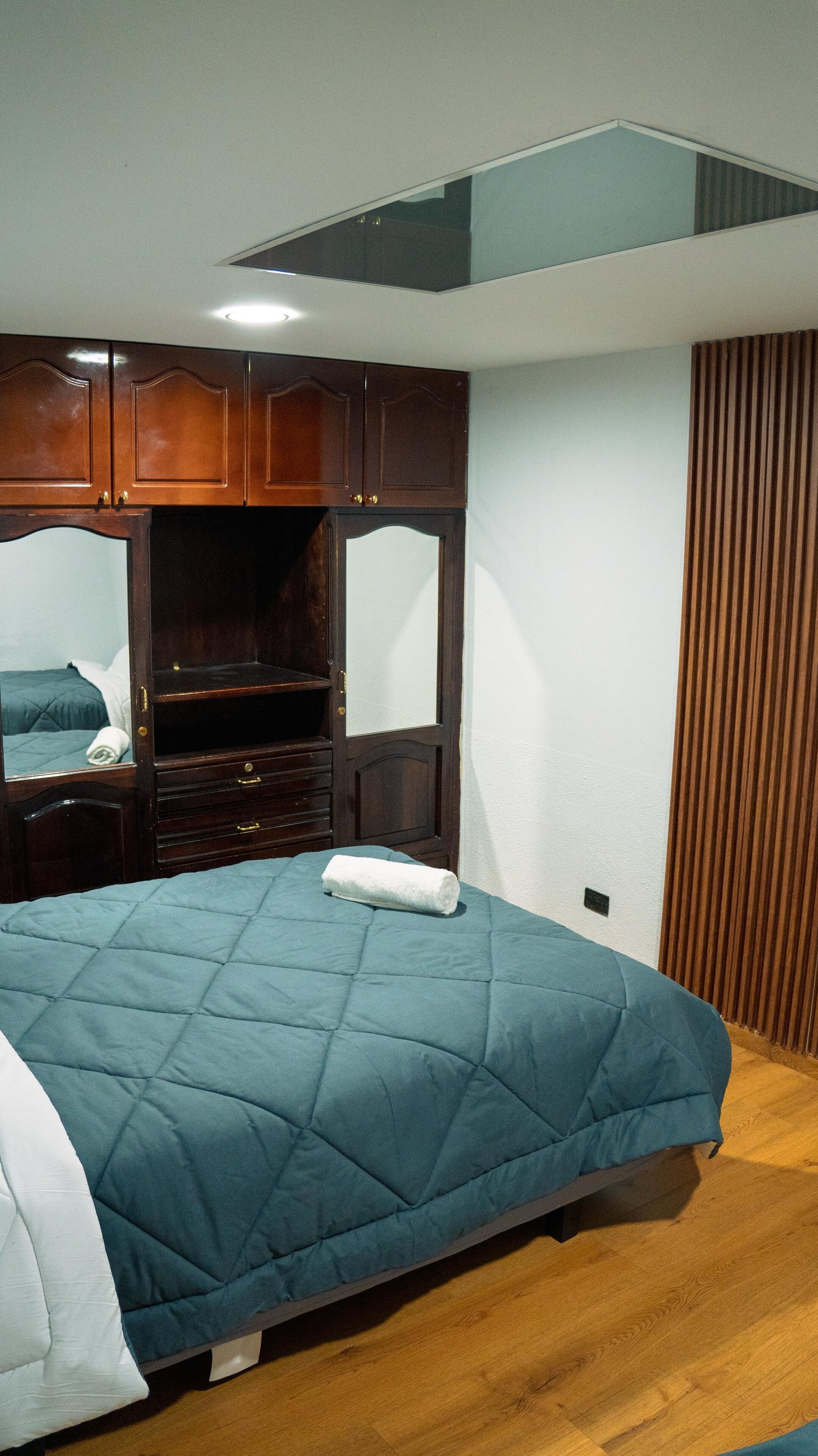 Quarto com cama, guarda-roupa de madeira e espelho.