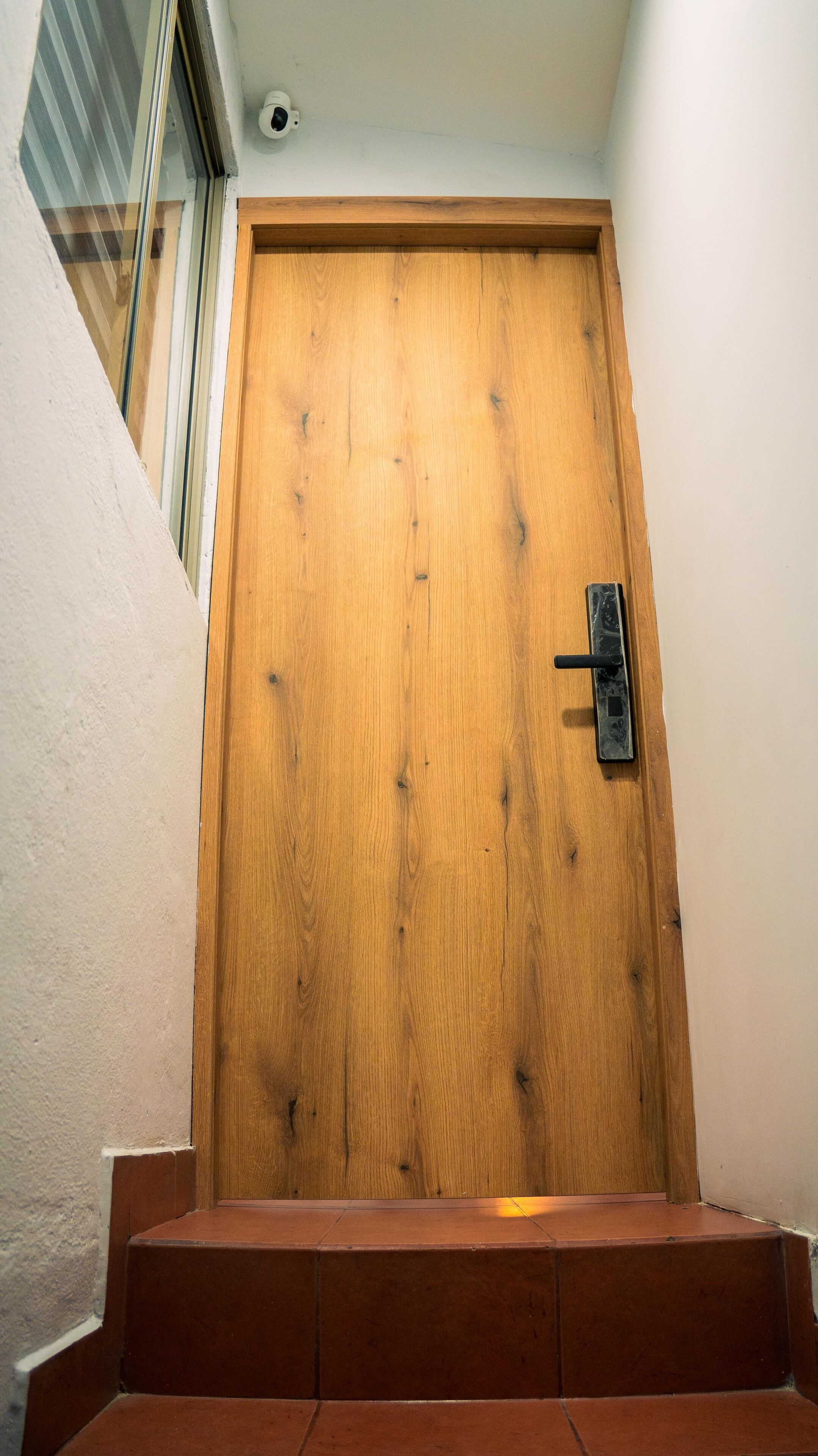 Une porte en bois, dotée d’une poignée, d’un judas et d’une petite fenêtre située au-dessus.