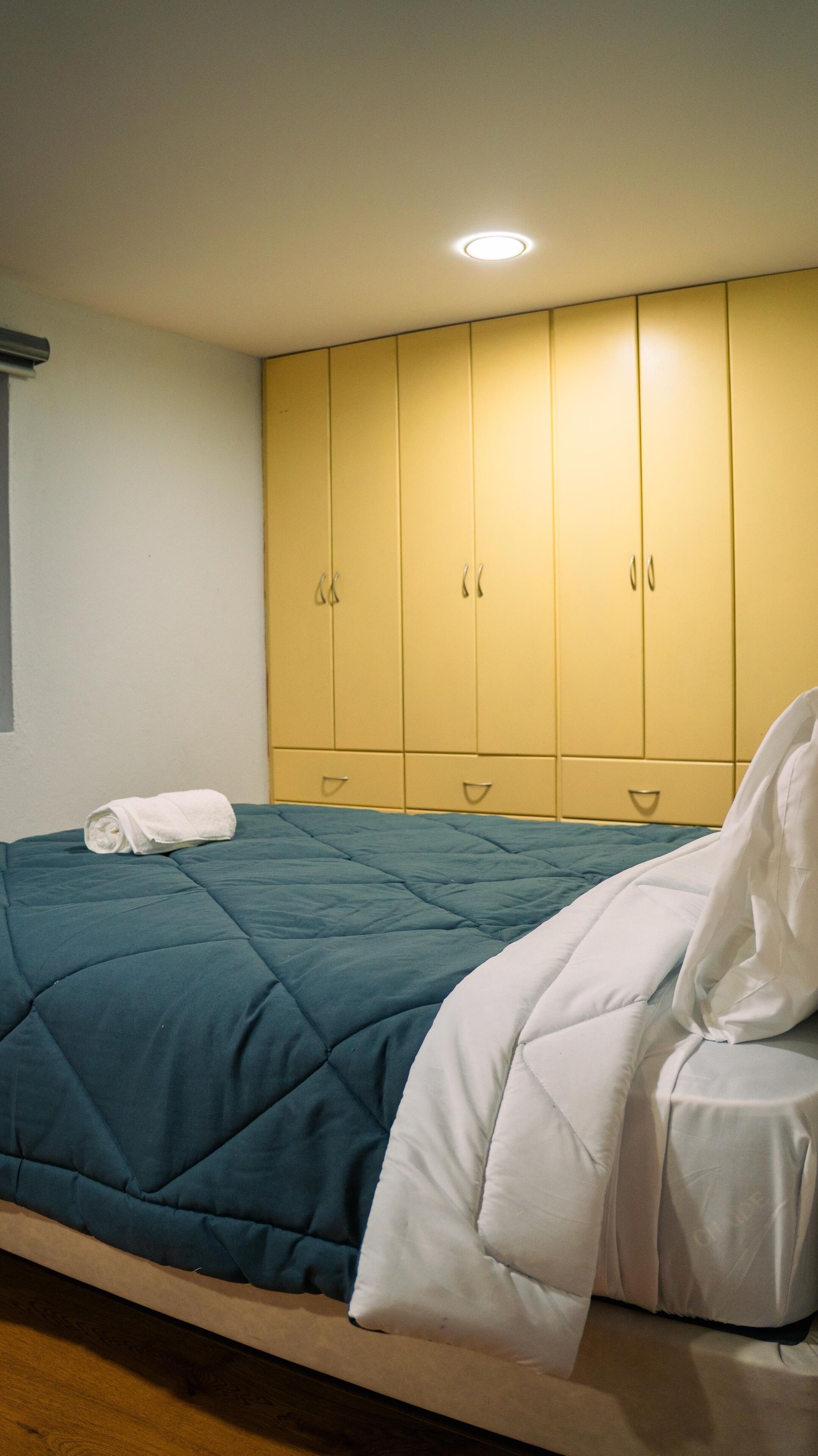 A neatly made bed with a blue and white duvet, a white towel, and a yellow wardrobe with multiple doors.
