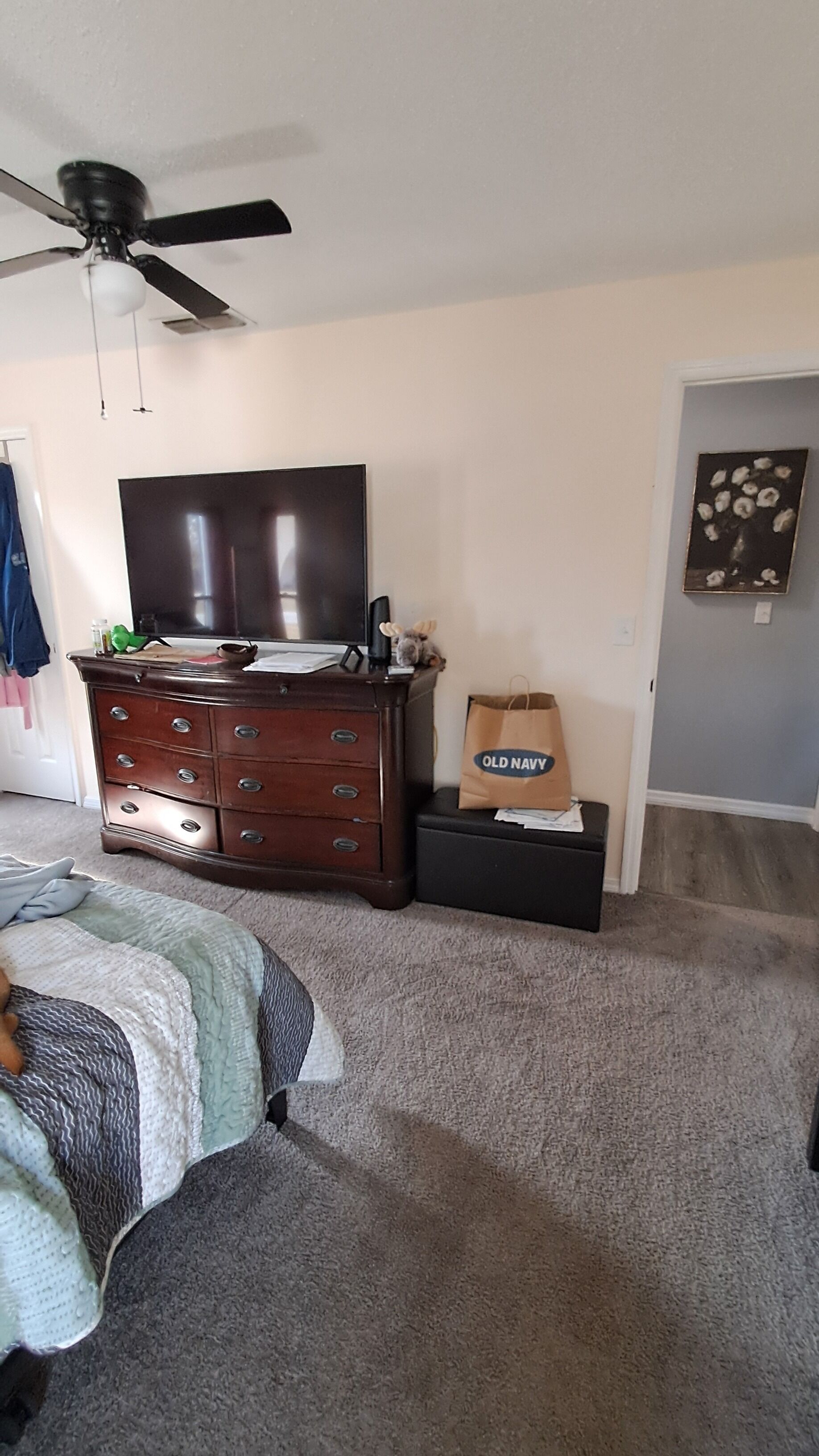 A bedroom with a bed, dresser, TV, ceiling fan, and a bag labeled "Old Navy".