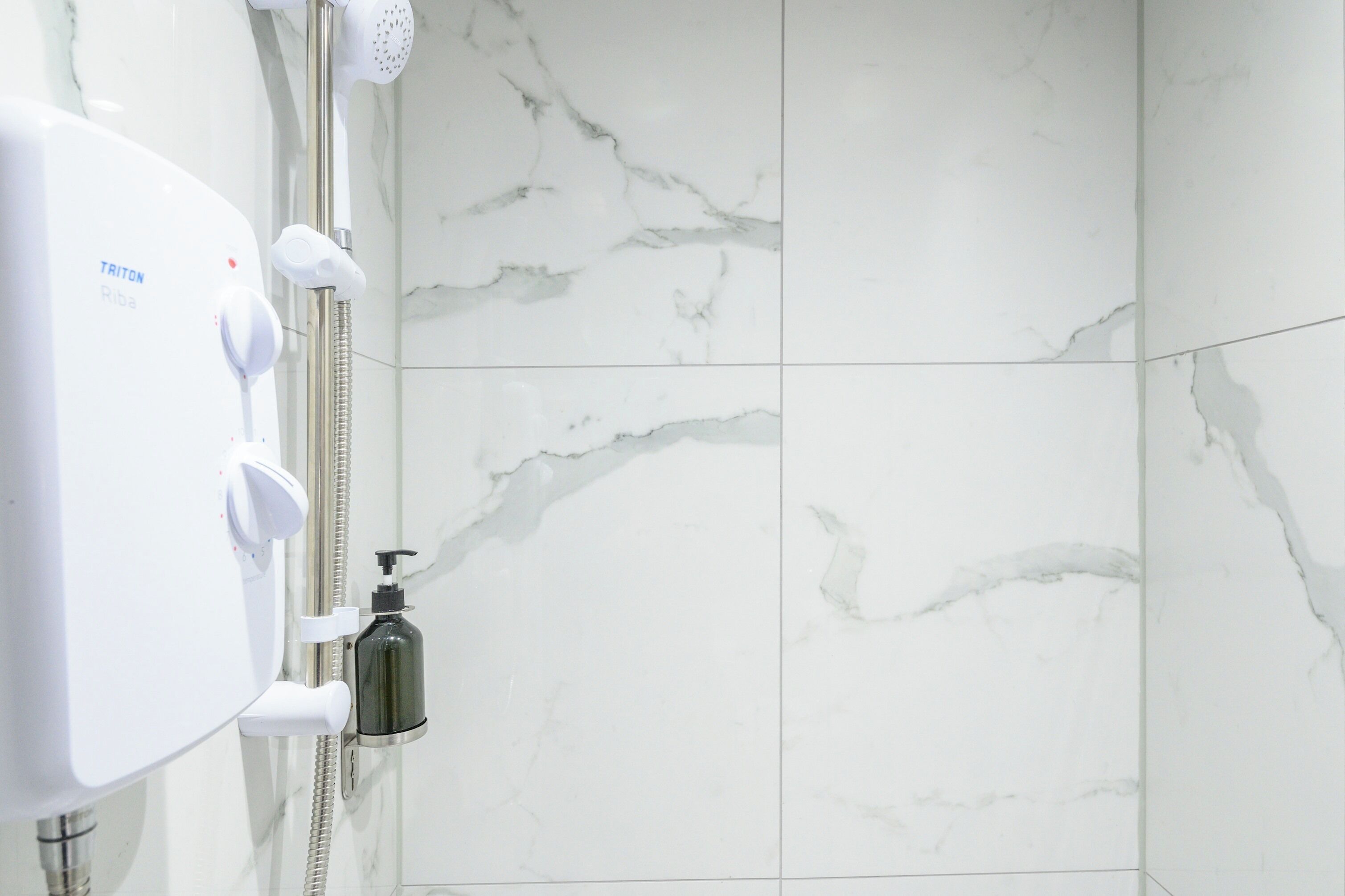 A bathroom with a white marble wall, a white shower unit, and a handheld showerhead.
