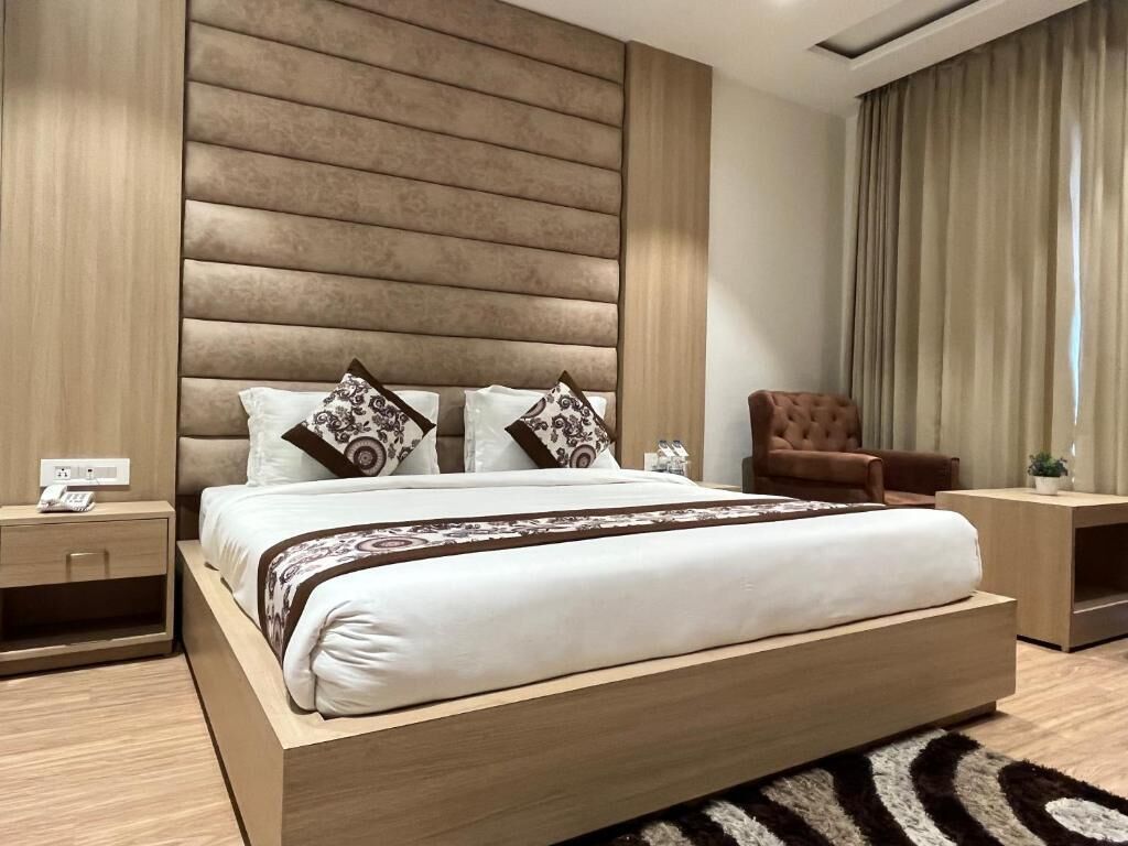 Une chambre à coucher moderne avec un grand lit, une tête de lit en bois, un fauteuil en cuir marron et une table de chevet avec une lampe.