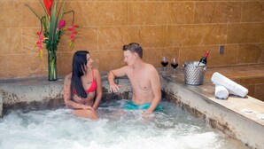 A couple in a hot tub with a vase of flowers and a bottle of wine on the side.