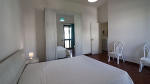Een slaapkamer met een bed, een kledingkast, een stoel en een spiegel.