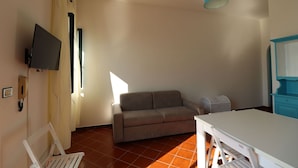Een ruime, goed verlichte kamer met een bank, een tafel en een aan de muur bevestigde televisie.