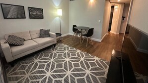 Een woonkamer met een bank, een kamerbreed tapijt, een eettafel met stoelen, en een gang naar een andere kamer.