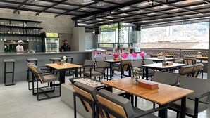 A café with tables and chairs, a bar area, and a view of the city. - Helena Building 1BR ✨ Jacuzzi + 360° Terrace in Medellín (Medellín)