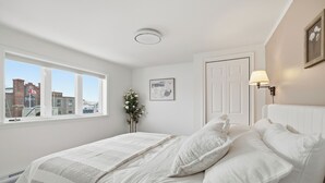 A bedroom with a large bed, a window with a city view, a door, and a wall-mounted lamp. - 5 mins walk from The Harbour, The Rooms, and all the fun of Downtown St. John’s! (St. John's)