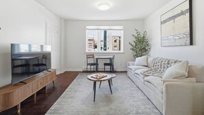 A modern living room with a flat-screen TV, a dining table with chairs, a sofa, and a large window offering a city view. - 5 mins walk from The Harbour, The Rooms, and all the fun of Downtown St. John’s! (St. John's)