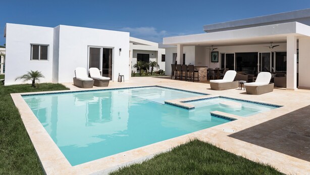 Un área de piscina moderna con piscina rectangular, sillas de descanso y una zona de estar cubierta.