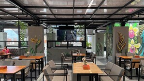 Un café moderne avec un plafond haut, de grandes fenêtres et des plantes d’intérieur.