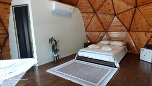 A bedroom with a bed, a small table, a potted plant, an air conditioning unit, and a wardrobe.