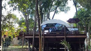 A treehouse with a white canopy and a purple umbrella, surrounded by dense forest.