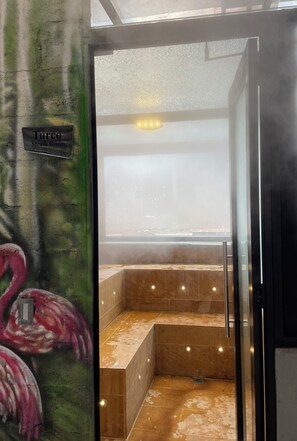 Ein Dampfbad mit einem Schild mit der Aufschrift 'Turco Steam Room', einem gefliesten Boden und einer Glastür.