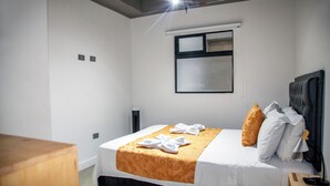 A hotel room with a bed, a wooden nightstand, a window, and a wall-mounted light fixture. - Modern 2BR Apartment in Helena ✨ Terrace, Jacuzzi & Café (Medellín)