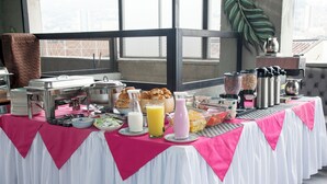A breakfast buffet with various food items and beverages, set up on a table with a pink and white tablecloth. - Modern 2BR Apartment in Helena ✨ Terrace, Jacuzzi & Café (Medellín)