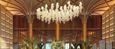 A spacious lobby with a modern chandelier, large potted plants, and a patterned floor.