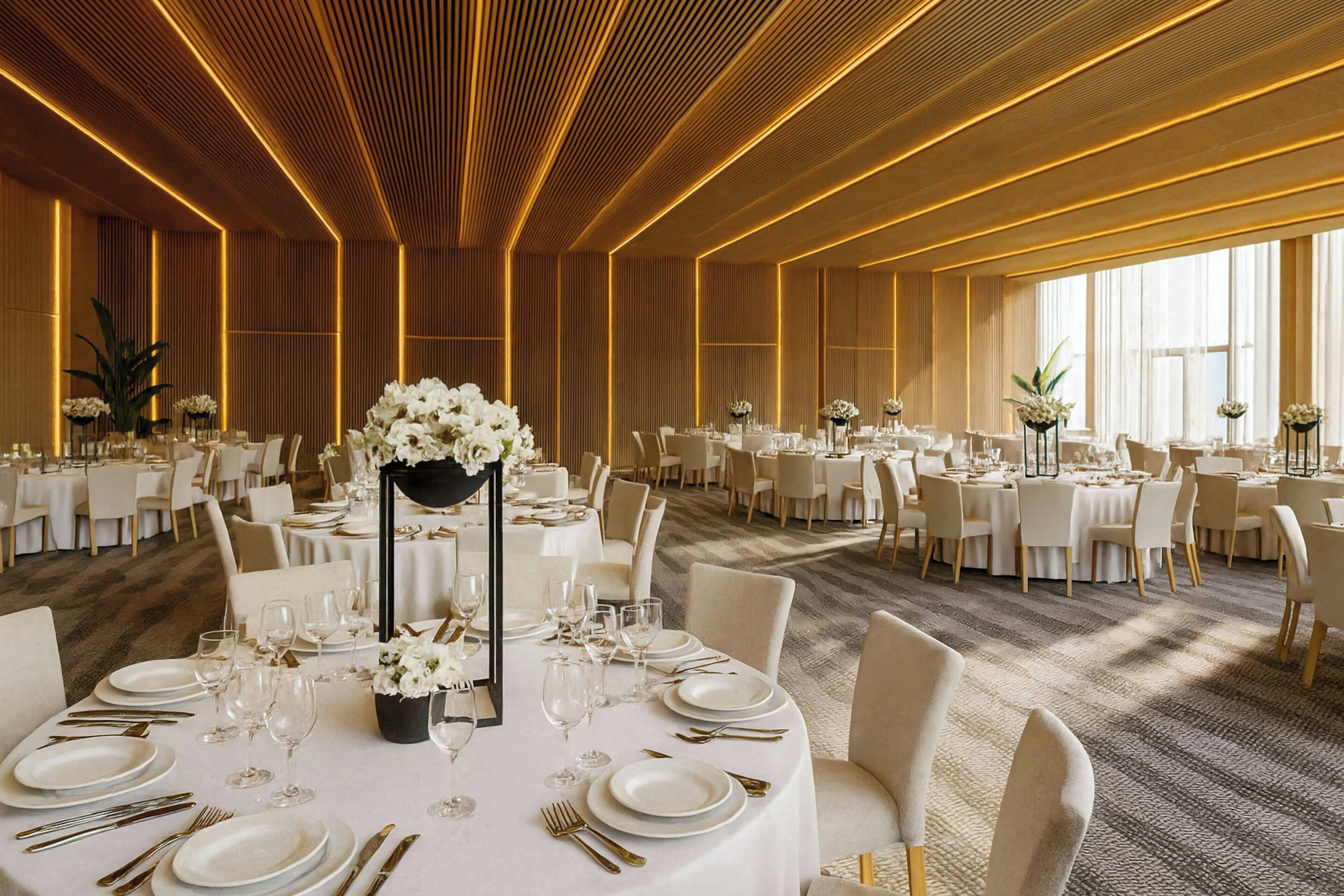 Une salle de banquet avec des tables rondes, des nappes blanches et des centres de table floraux.