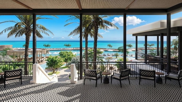 A covered outdoor area with a view of the ocean, palm trees, and lounge seating. - The Pyrmont Curaçao, An Autograph Collection, All-Inclusive Resort Adults Only (Willemstad)