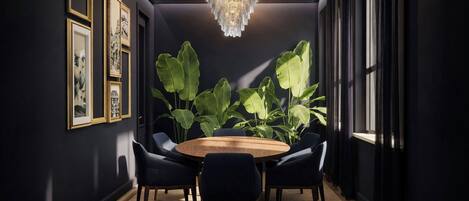 A dark room with a round wooden table, six chairs, and large green plants.