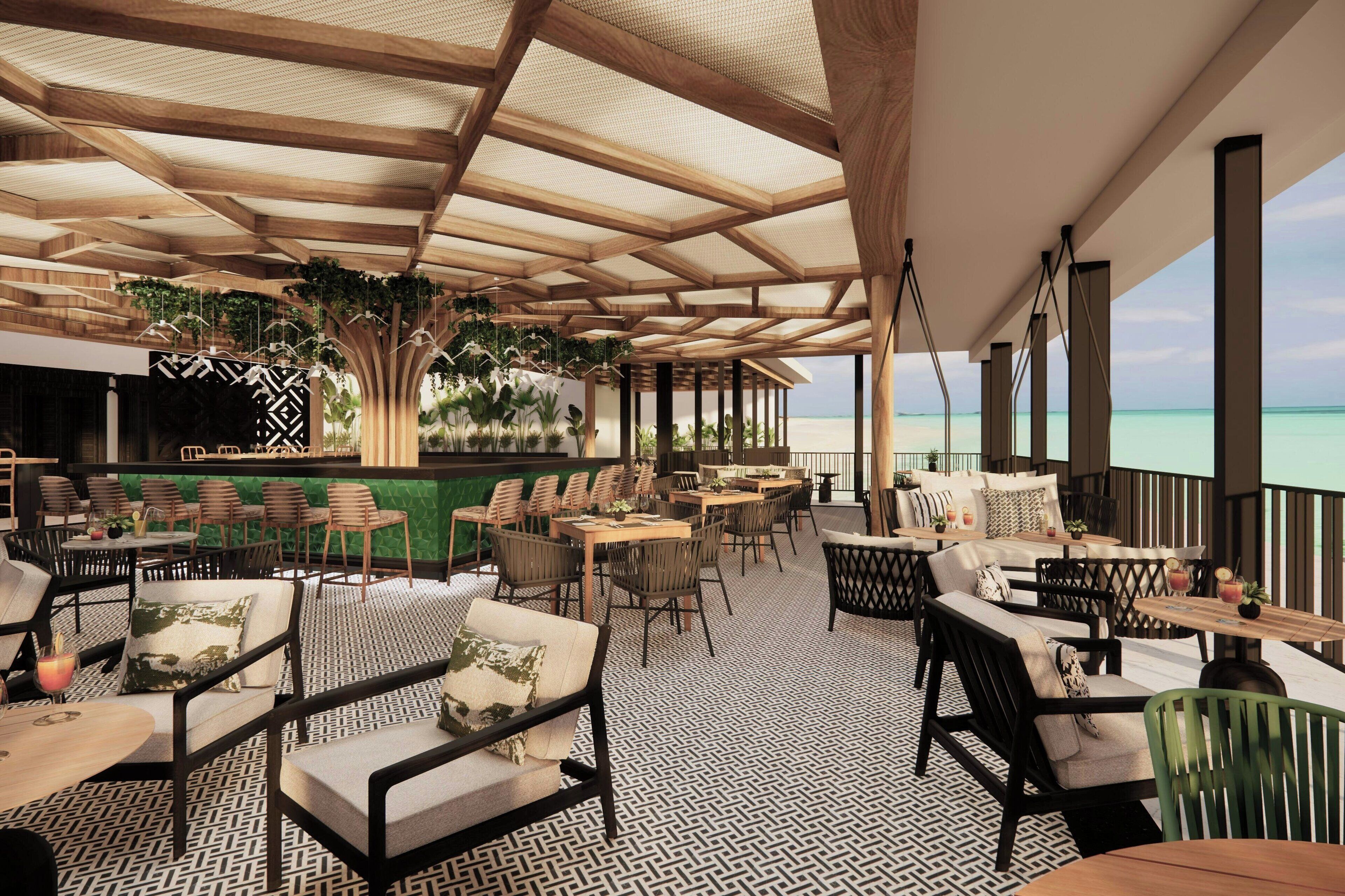 A spacious outdoor seating area with wooden tables and chairs, a patterned floor, and a view of the ocean.