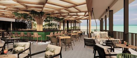 A spacious outdoor seating area with wooden tables and chairs, a patterned floor, and a view of the ocean.