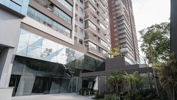 Un edificio moderno con facciata in vetro riflettente, numerosi balconi e un'area d'ingresso curata con verde.
