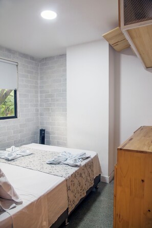 Ein Schlafzimmer mit Bett, Fenster, einem Holztisch und einer Ziegelwand.