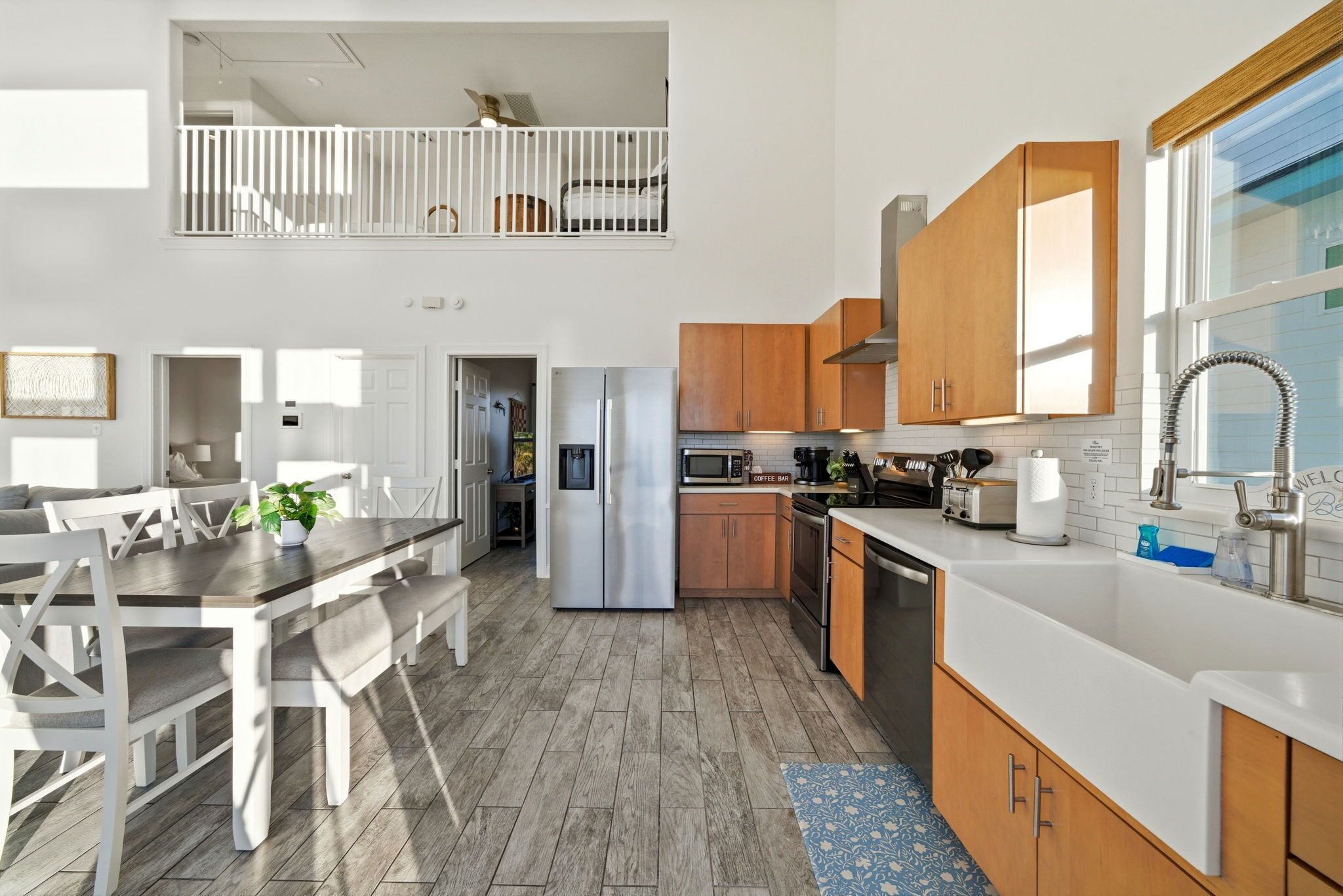 A modern kitchen with a dining area, wooden cabinets, stainless steel appliances, and a view to a balcony.