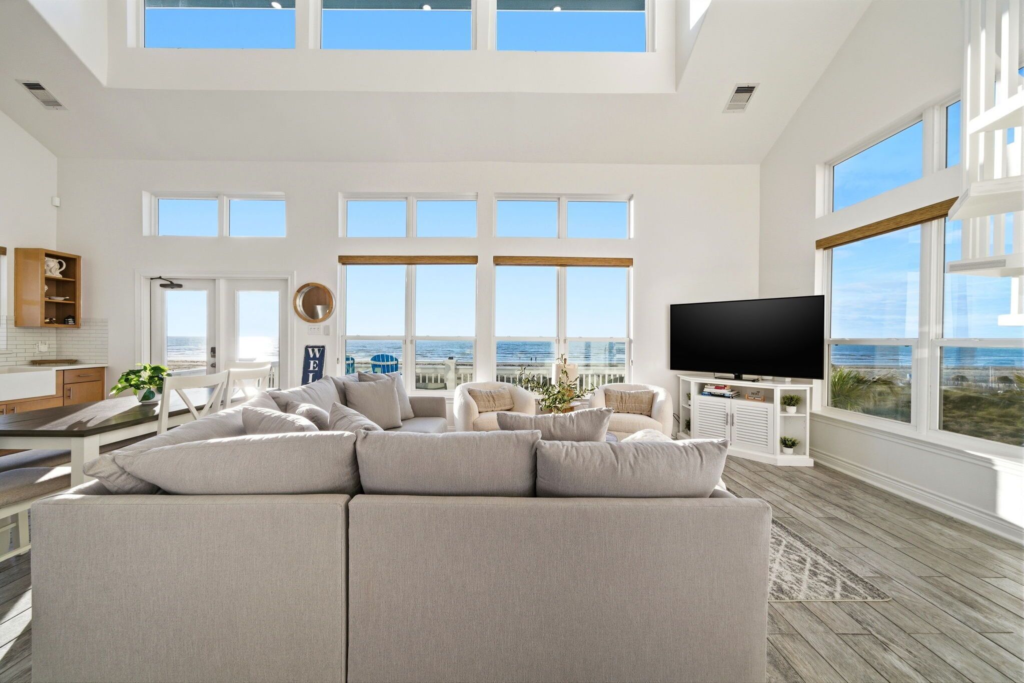 A spacious living room with a large sectional sofa, a flat-screen TV, and a view of the ocean through large windows.