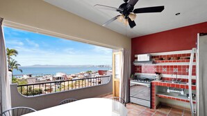 Ein Balkon mit Blick auf den Ozean und die Stadtlandschaft, eine Küche mit roten und weißen Fliesen und ein Essbereich mit Tisch und Stühlen.