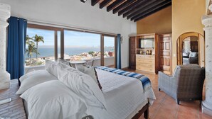 Ein Schlafzimmer mit einem großen Bett, Meerblick und einem Balkon mit Tisch und Stühlen.